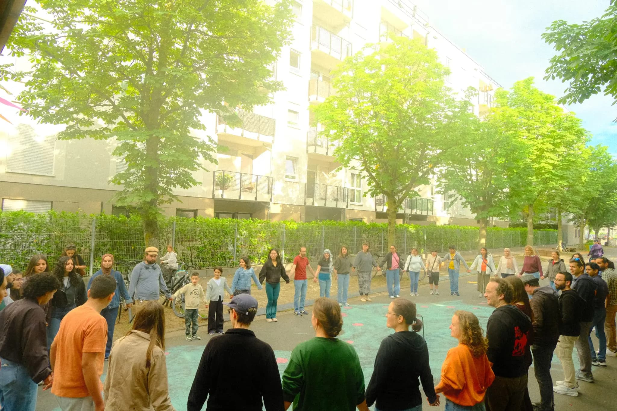 Eine Gruppe hält sich in einem großen Dabke-Kreis draußen unter Bäumen an den Händen.