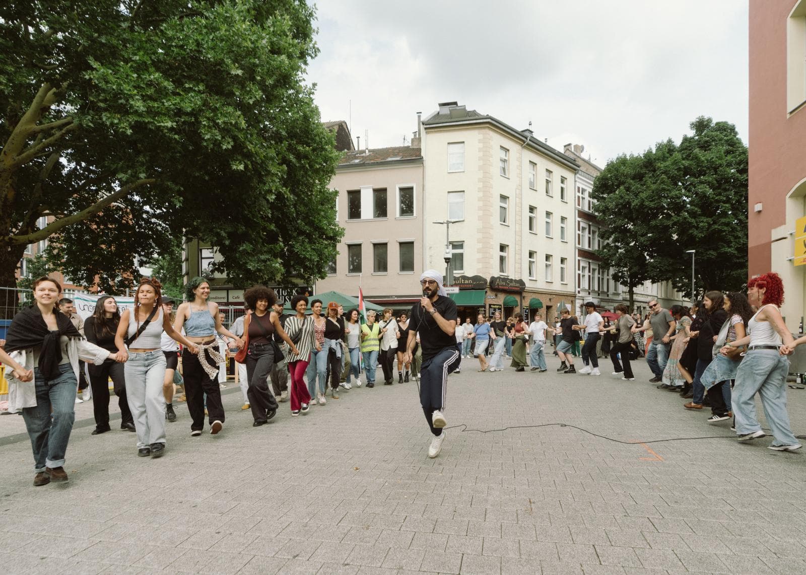 Eine große Community-Gruppe tanzt draußen Dabke mit einem YallaDabka-Facilitator